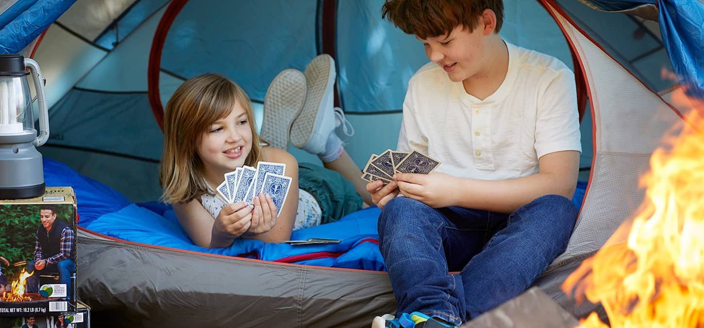 A boy and a girl are playing cards in a tent with a fire in the fire pit
