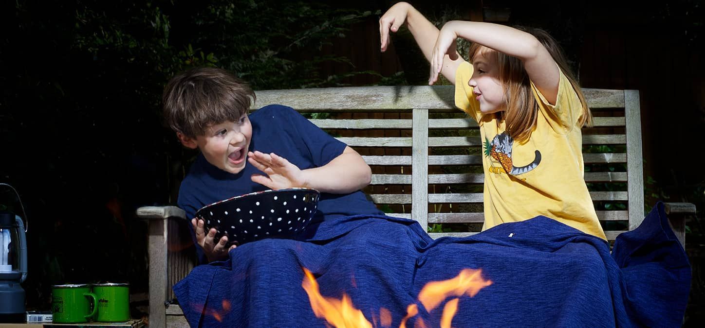 A boy and a girl are sitting next to a fire pit eating popcorn telling ghost stories