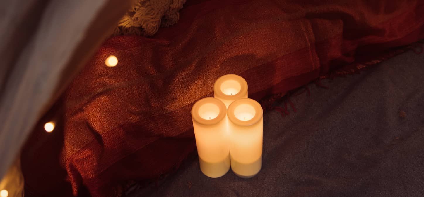 closeup of three candles are lit in a camping tent.