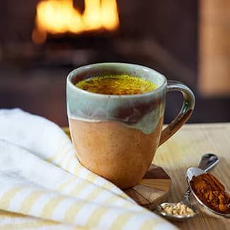 Mug of golden almond milk latte with a cozy fireplace backdrop.