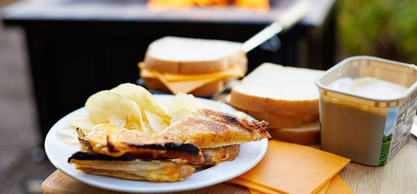 A grilled cheese sandwich on a plate with chips in front of a fire pit