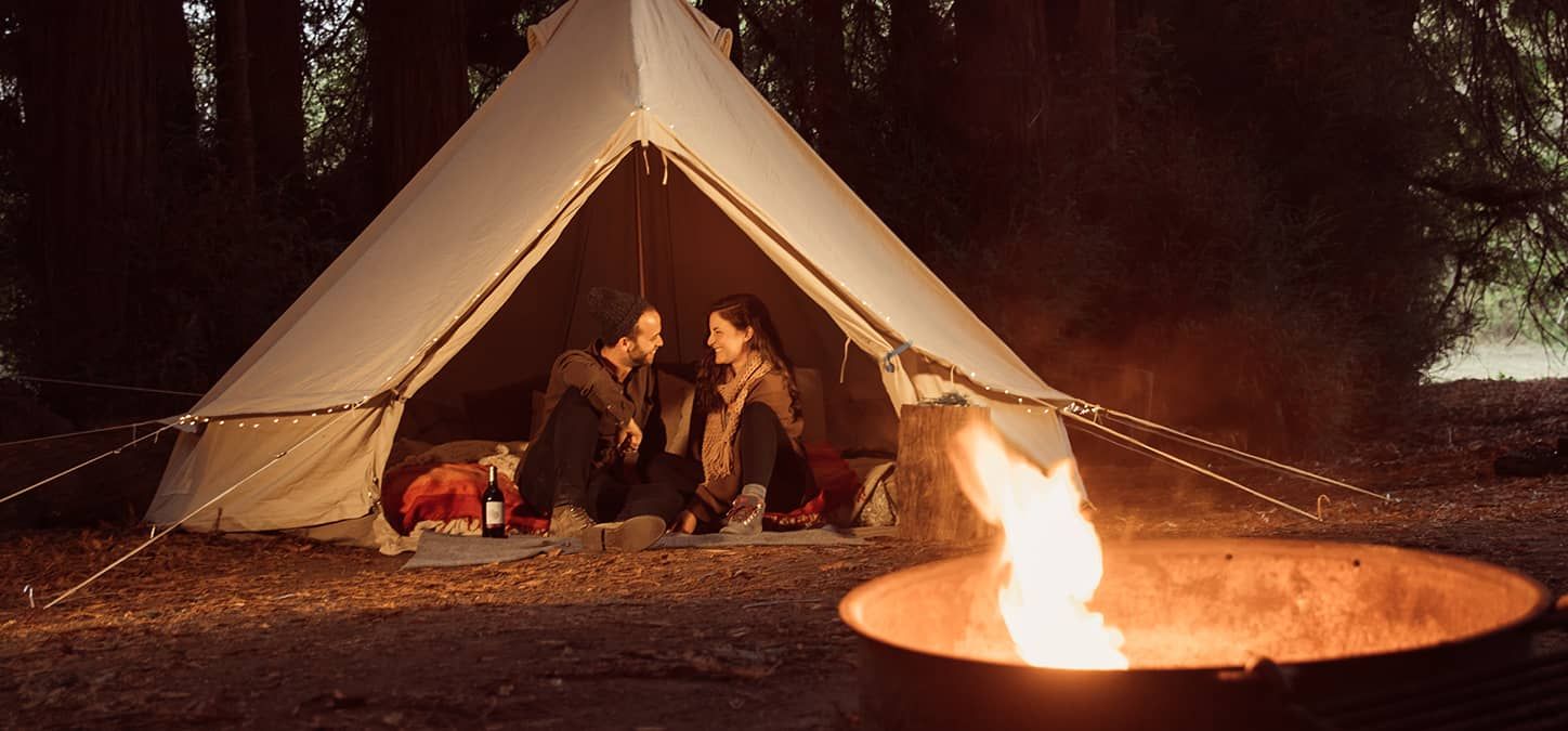 A couple is sitting in a tent next to a fire pit.