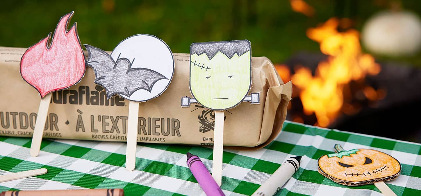 A table topped with a checkered tablecloth , crayons , and paper crafts with fire pit in background