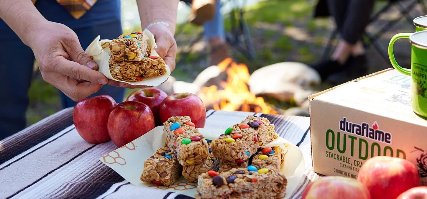 A person is holding a homemade granola bars in front of a fire pit.