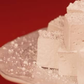 A close up of homemade marshmallows on a plate covered in powdered sugar.