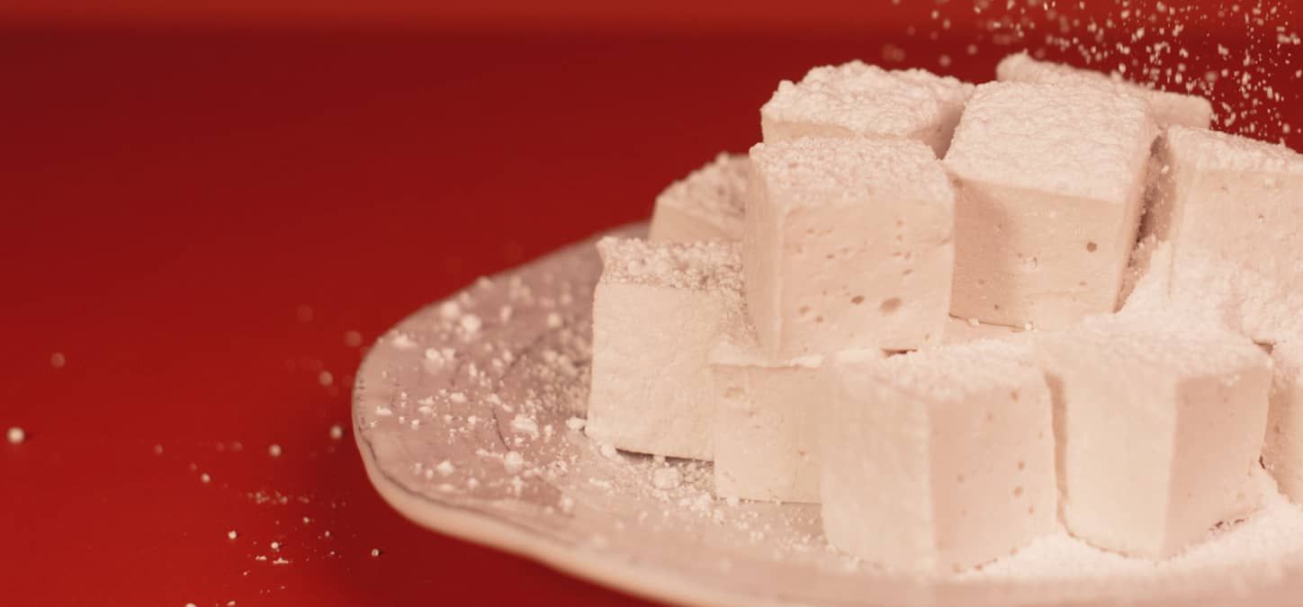A plate of marshmallows covered in powdered sugar on a red table.