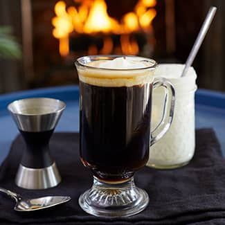 Irish coffee in a glass mug with whipped cream, next to a jar of cream and a jigger.