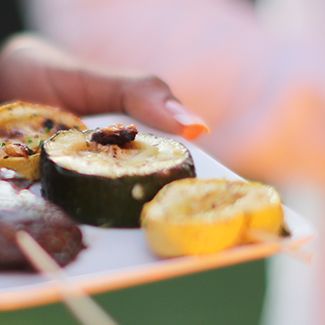 Hand holding a plate of grilled vegetables: zucchini, squash, and other vegetables.