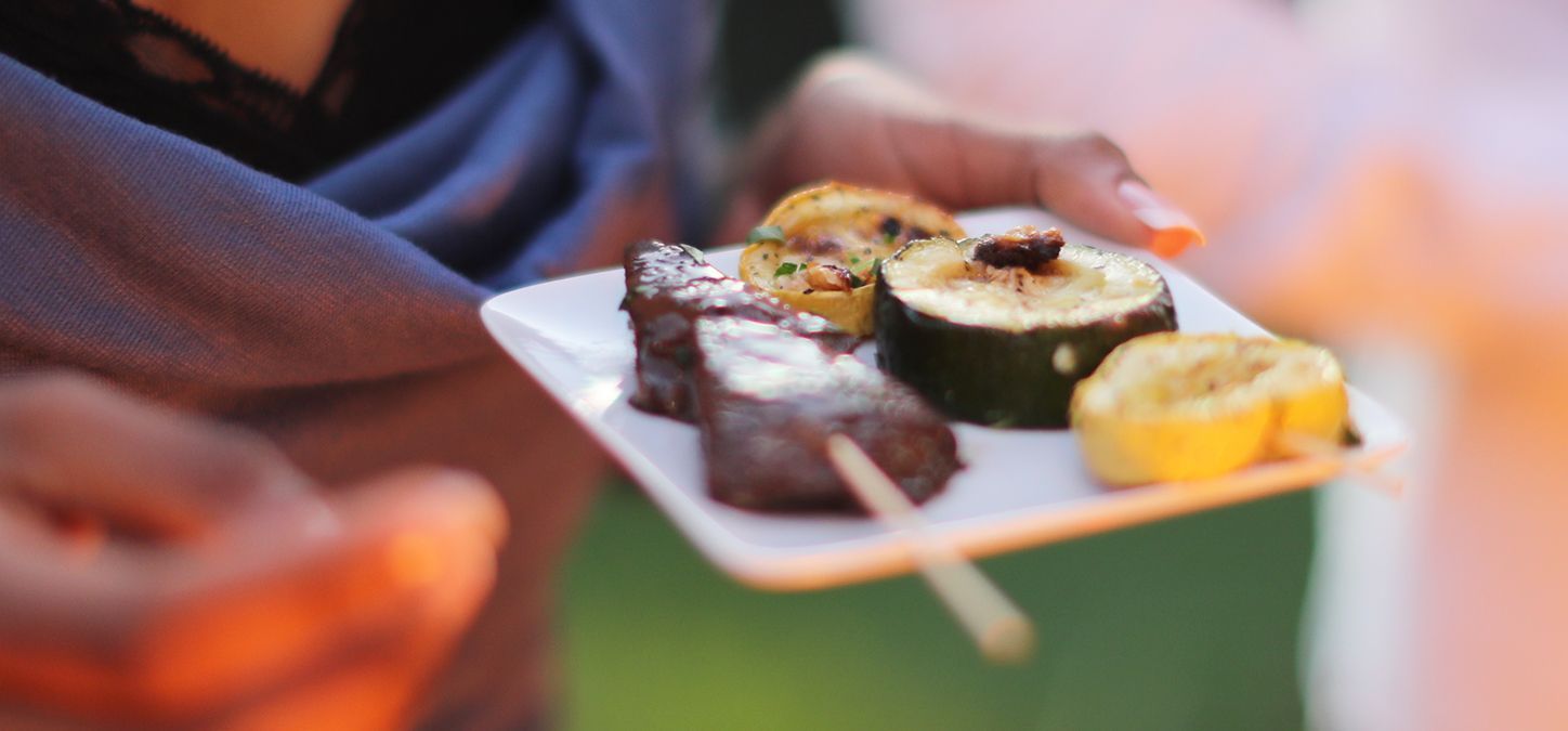 A person is holding a plate of food on a stick.