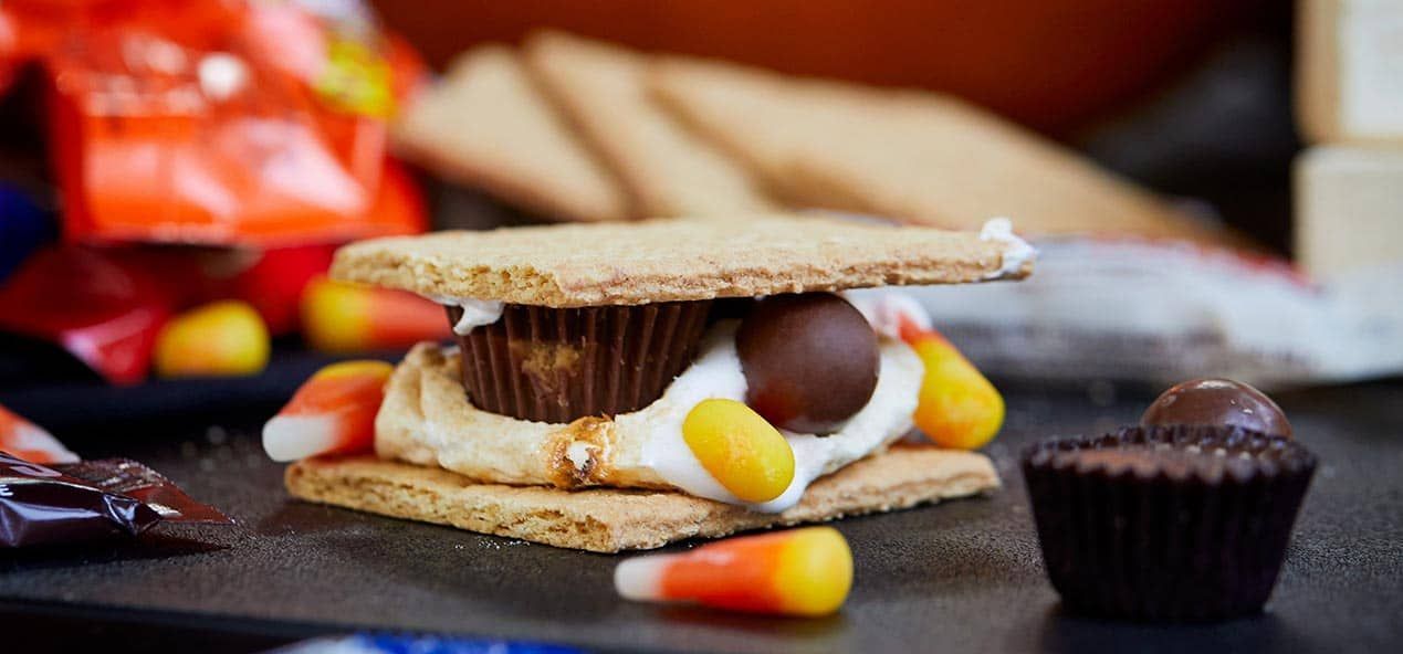 A s'more with candy corns, marshmallows and a peanut butter cup on a table.