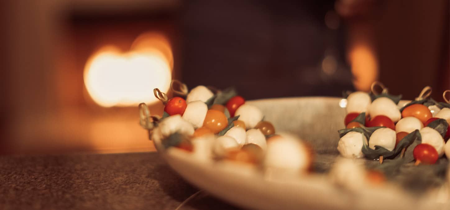A close up of a plate of mozarella and tomato skewers are on a marble counter with a fireplace in the background.