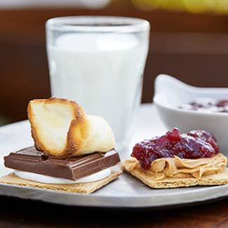 An open-faced PB&J s'mores with glass of milk on a table.