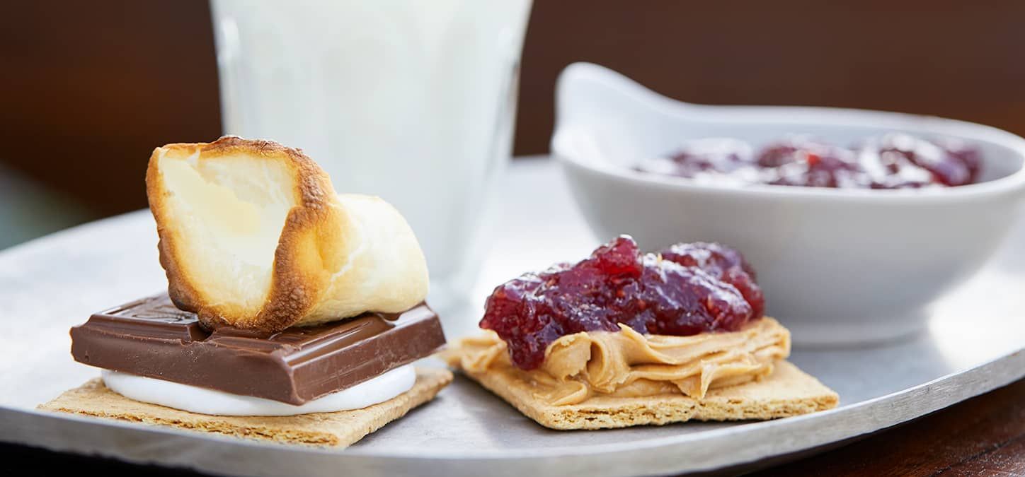 A white plate topped with an open-faced PB&J s'mores , and a glass of milk.