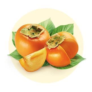 Two ripe, orange persimmons and a wedge of sliced persimmon resting on green leaves against a pale circular background.