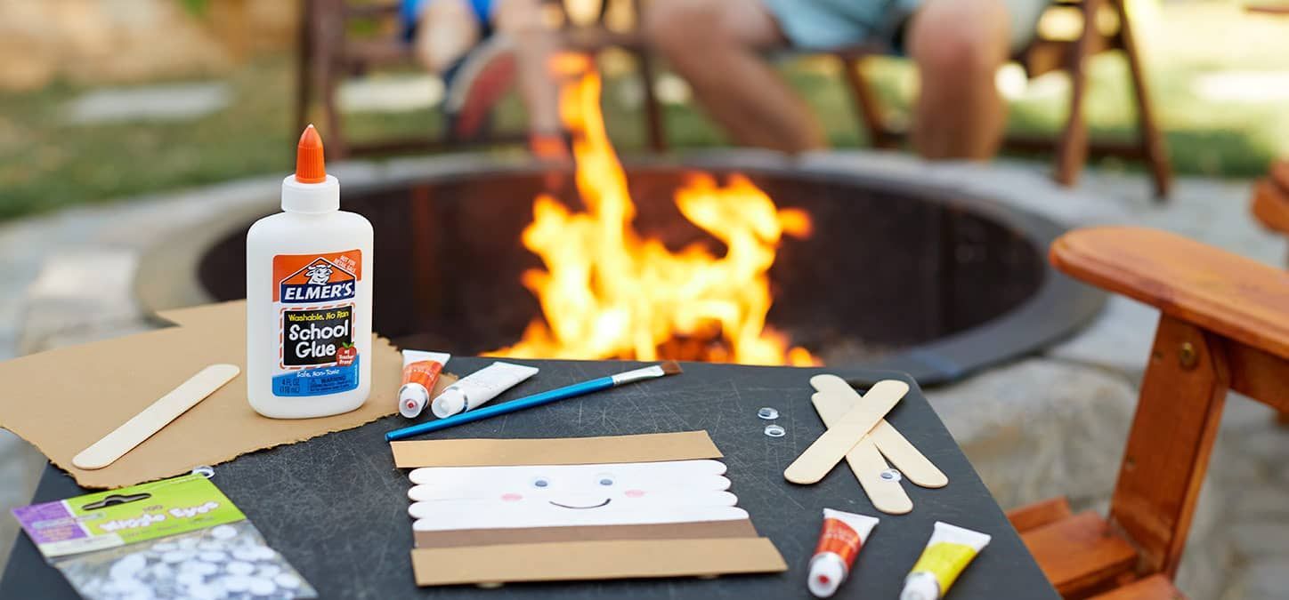 Craft items for making popsicle stick s'mores is sitting on a table next to a fire pit.
