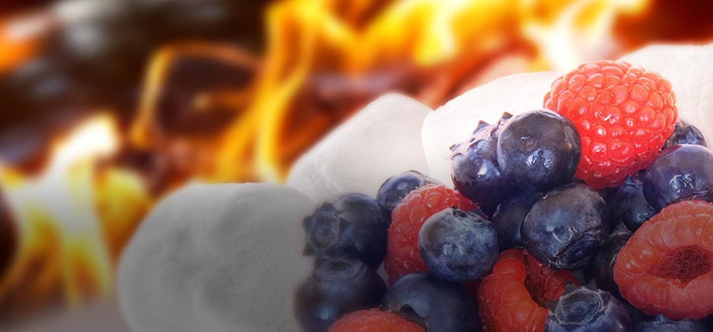 A close up of berries and marshmallows with a fire in the background.
