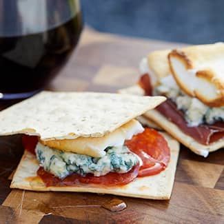Savory smores with cheese and salami on a cracker with a glass of wine in the background.