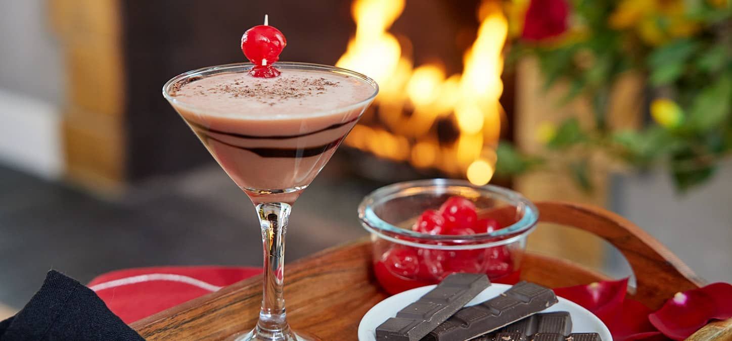 A chocolate cherry martini with a cherry on top is sitting in front of a fireplace