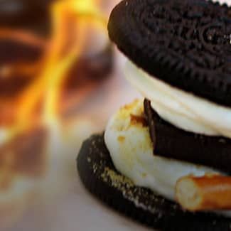 A close up of a s'moreo sandwich with a fire in the background.