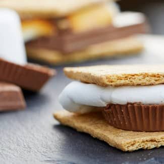 A close up of a s'mores sandwich with roasted marshmallows and peanut butter cup