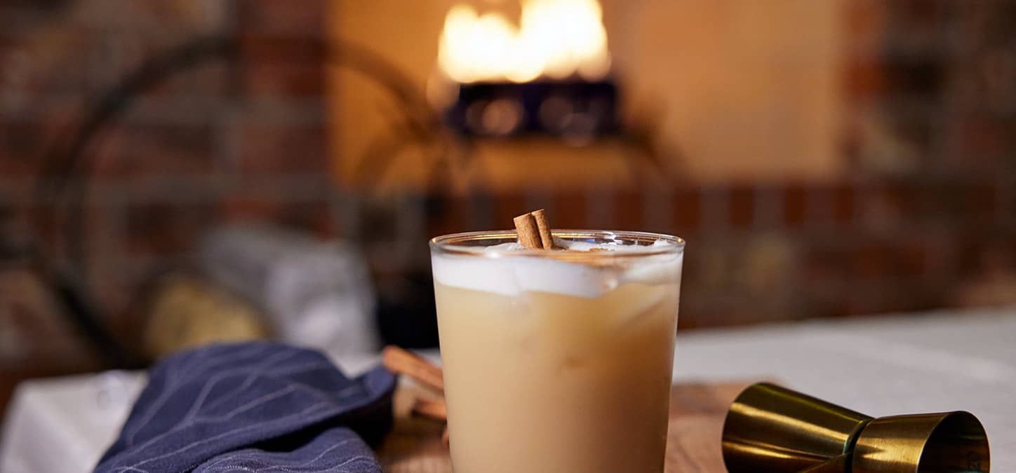 A spiced chai cocktail on a table ion front of a fireplace