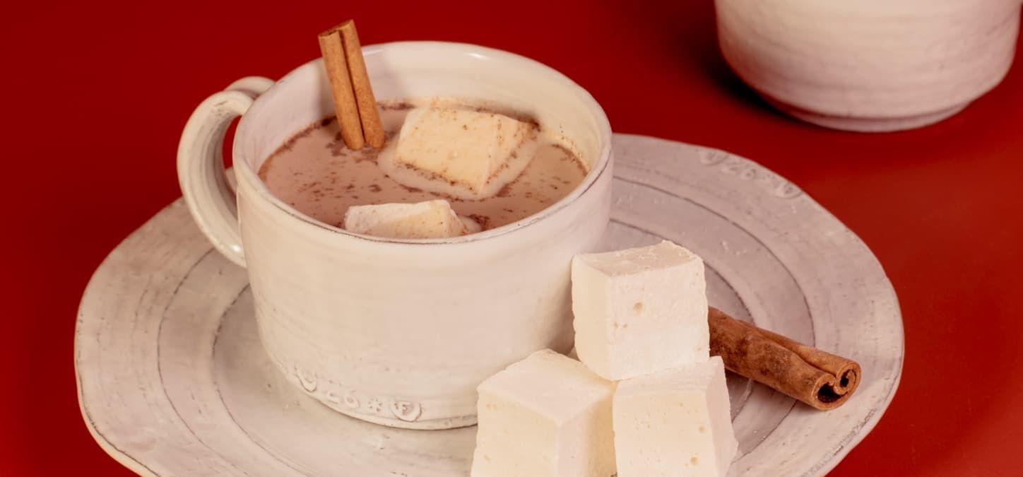 A cup of hot chocolate with marshmallows and cinnamon sticks on a plate.