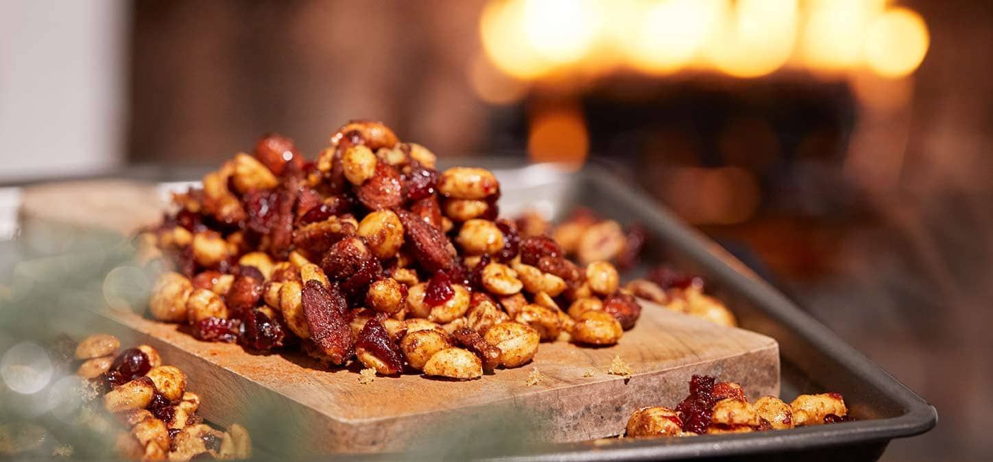 A pile of spiced mixed nuts is sitting on top of a wooden block in front of a fire.