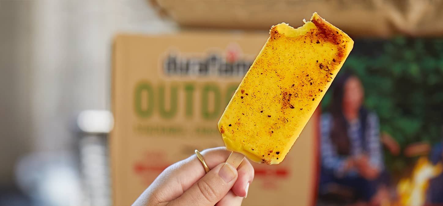 A person is holding a popscicle on a stick with a bite taken out of it.
