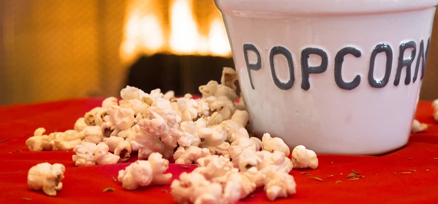 A bucket of popcorn is sitting on a red table in front of a fire