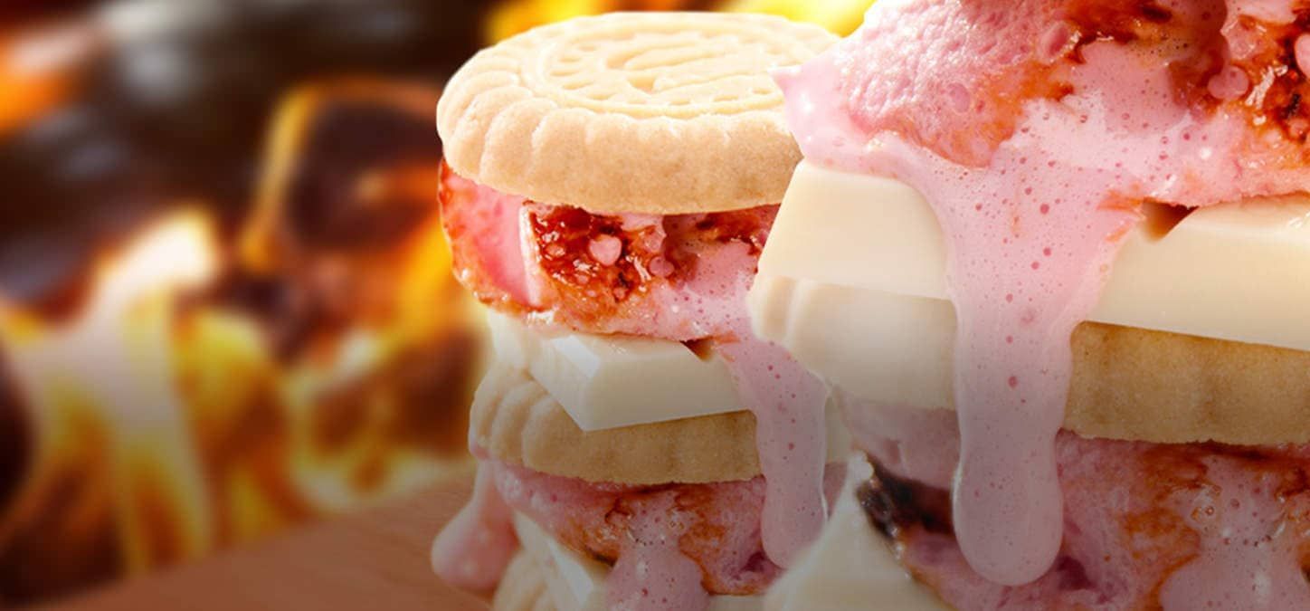 A close up of a strawberry shortcake s'mores sandwich with a fire in the background.