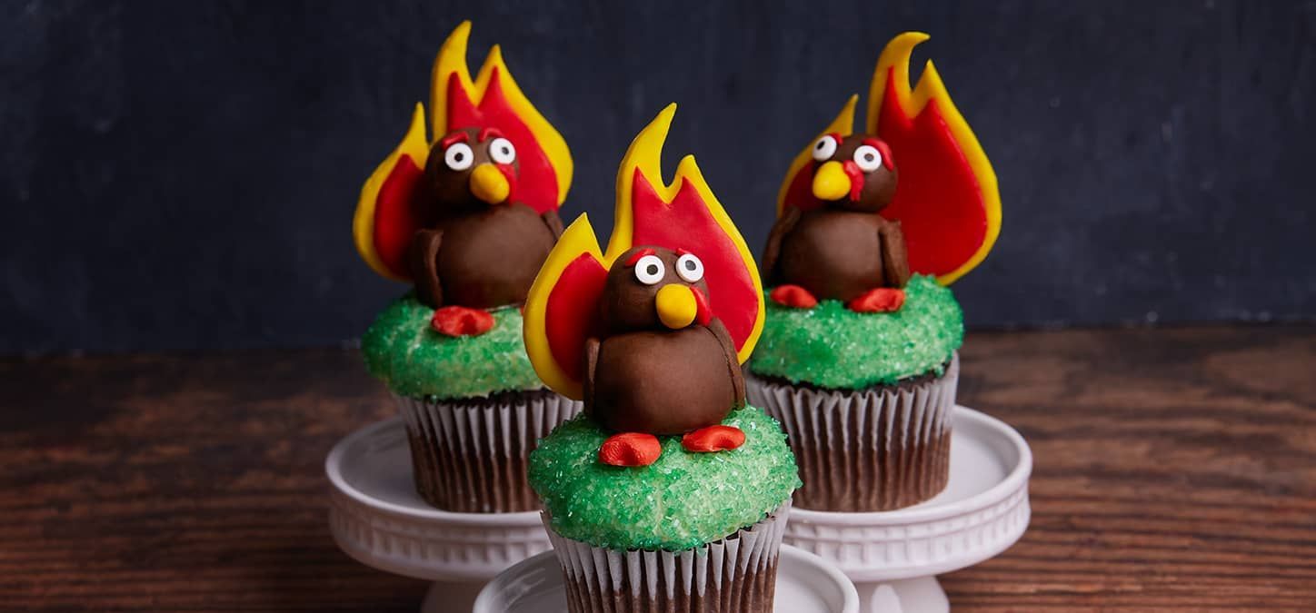 Three turkey cupcakes with fire-shaped tail decorations on a white cake stand.