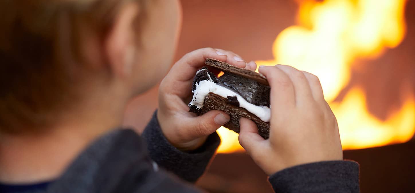 A child is eating a s'more in front of a fire.