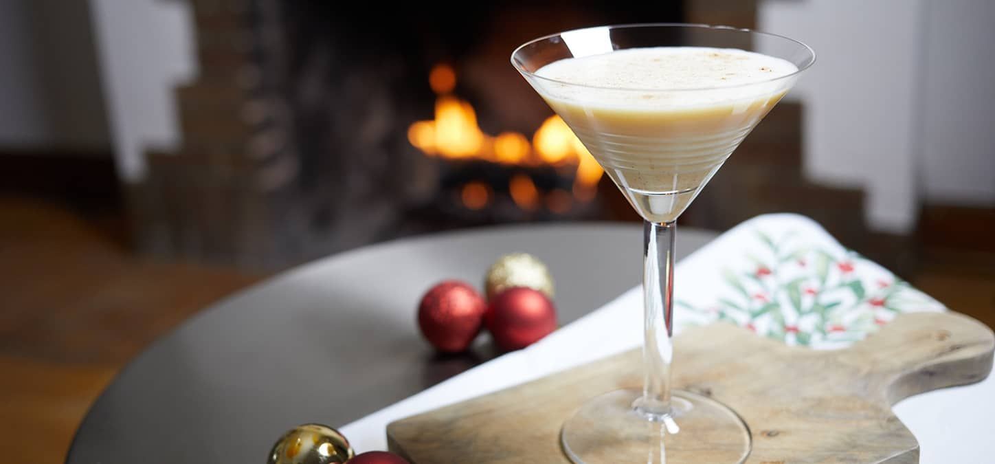 A whit christmas martini glass is sitting on a table in front of a fireplace.
