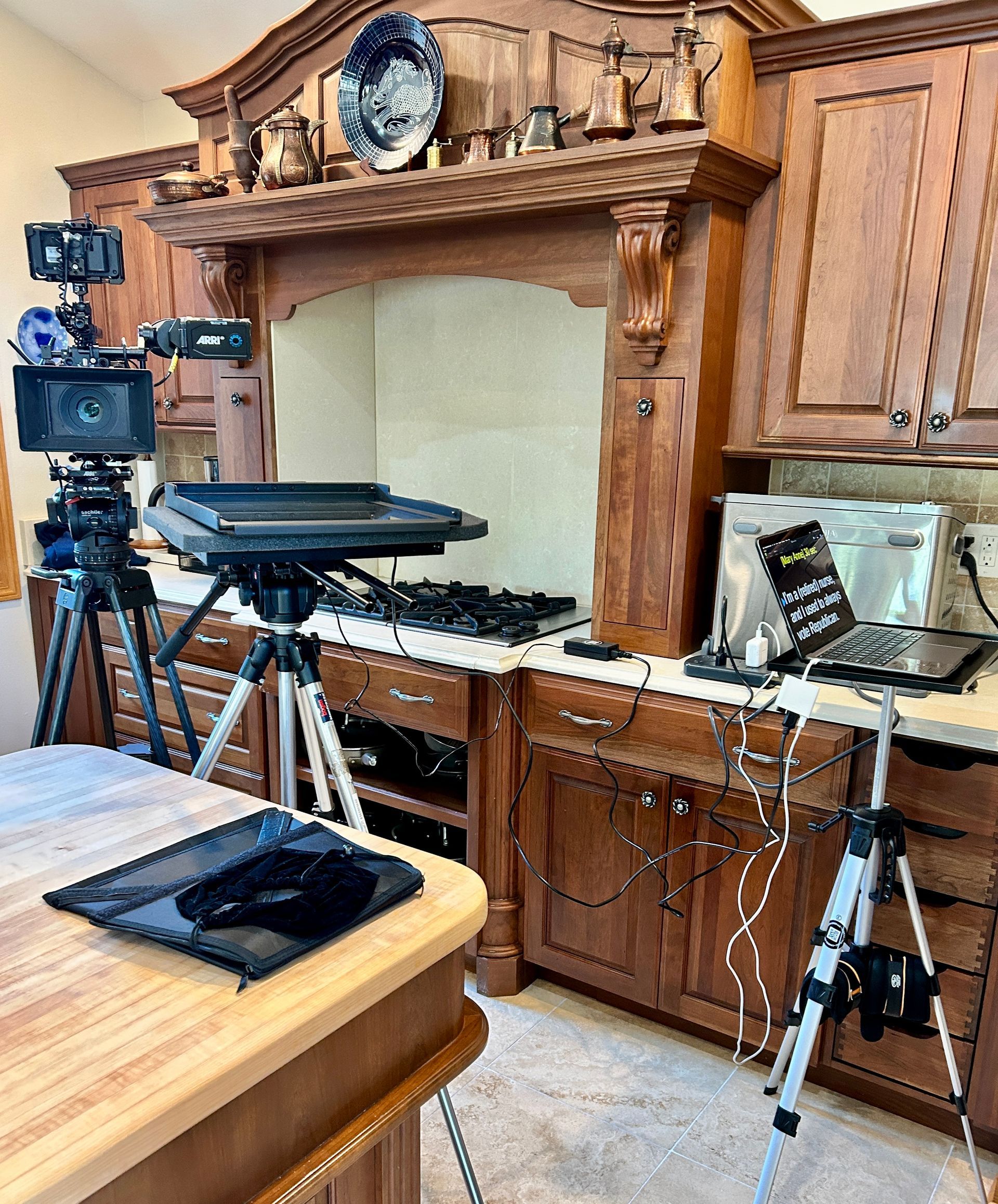 A kitchen set up for filming with multiple cameras on tripods, lighting equipment, and a laptop on a counter.