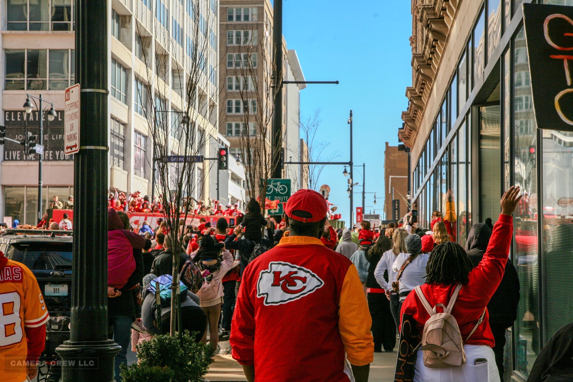 Fans wearing Kansas City Chiefs apparel cheer along a city street during a parade.