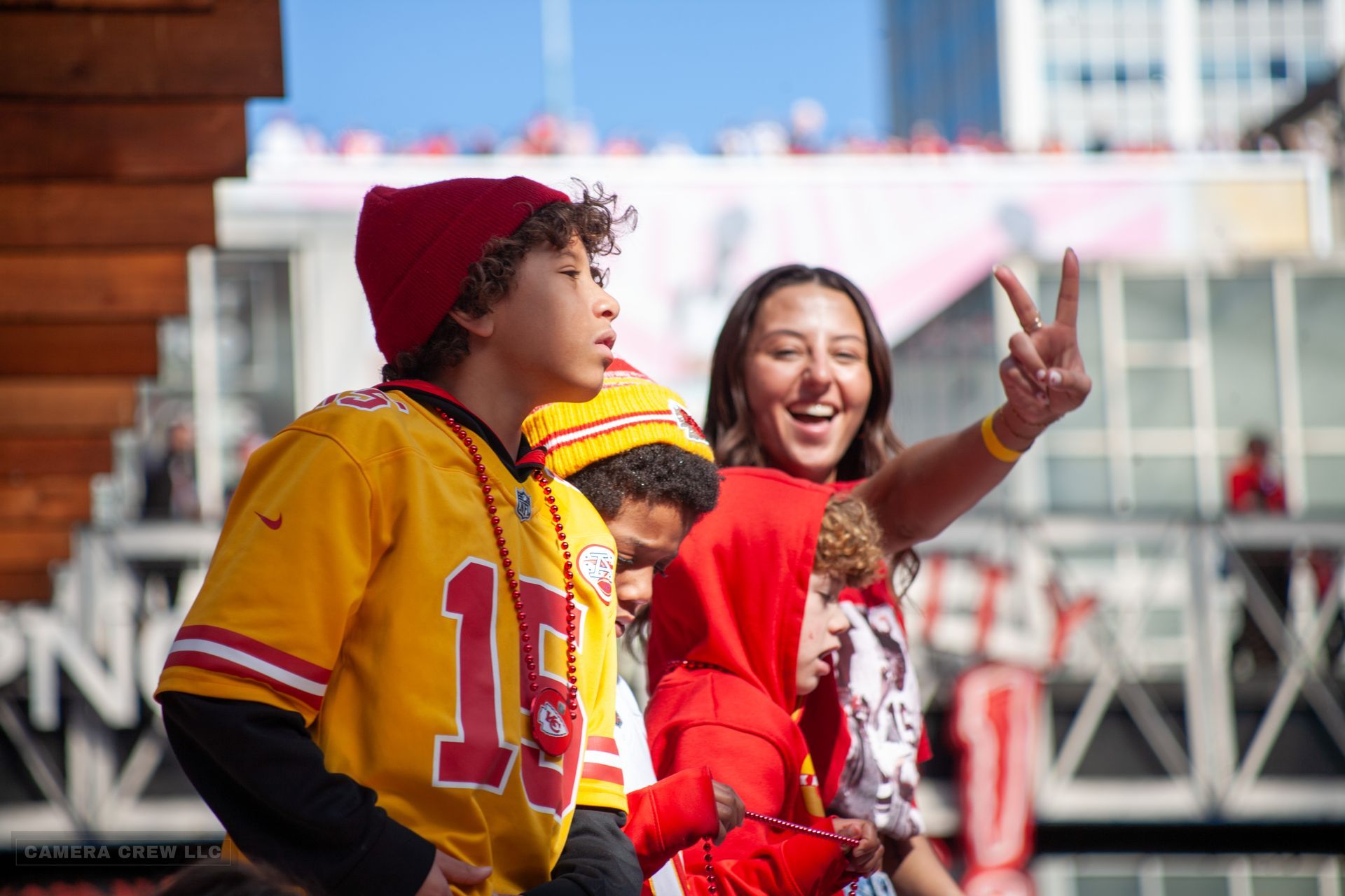 A group of people wearing red and yellow Chiefs gear, with one person making a peace sign, at a sunny outdoor event.