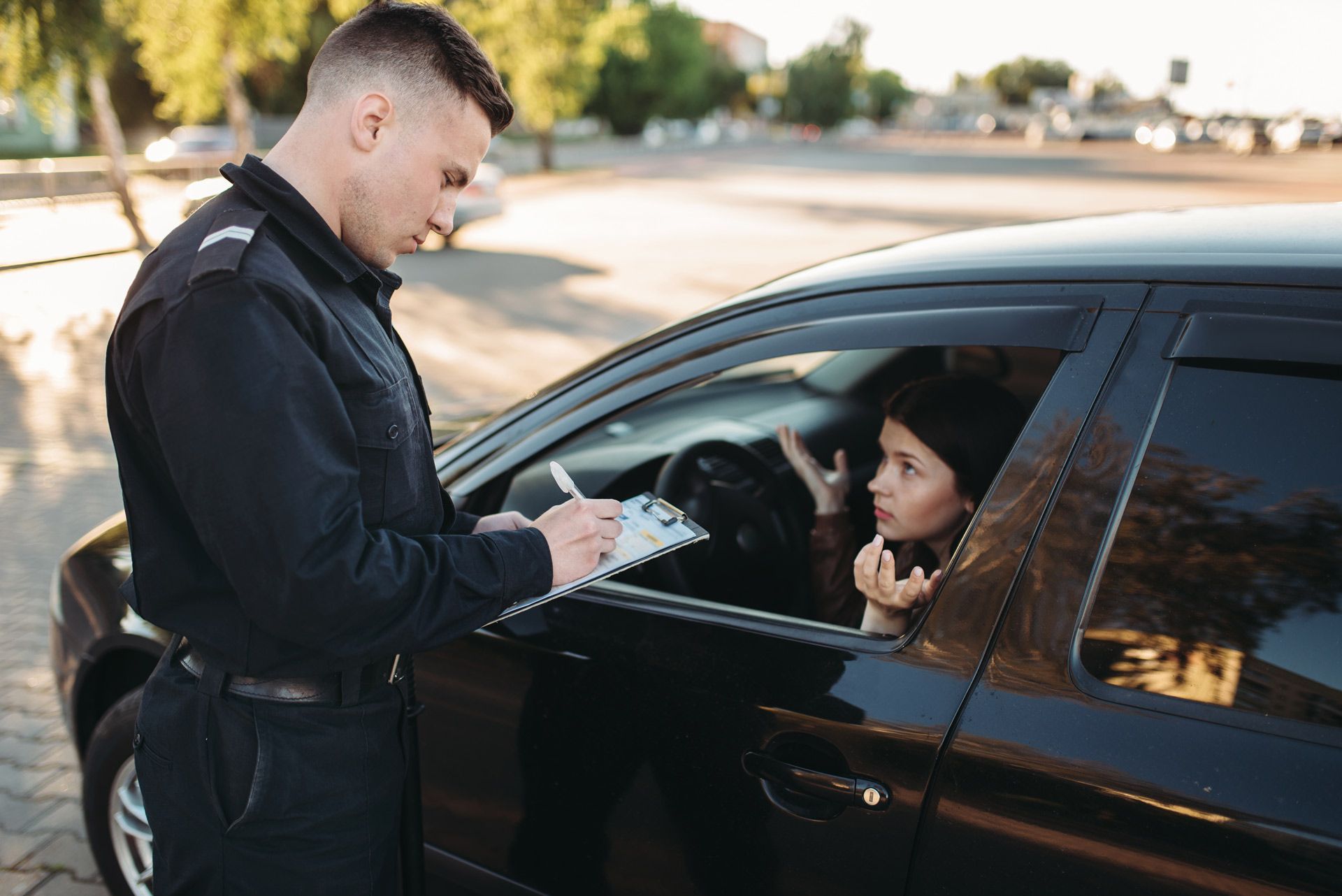 Police officer writing a ticket for a woman in a car. The woman looks upset.