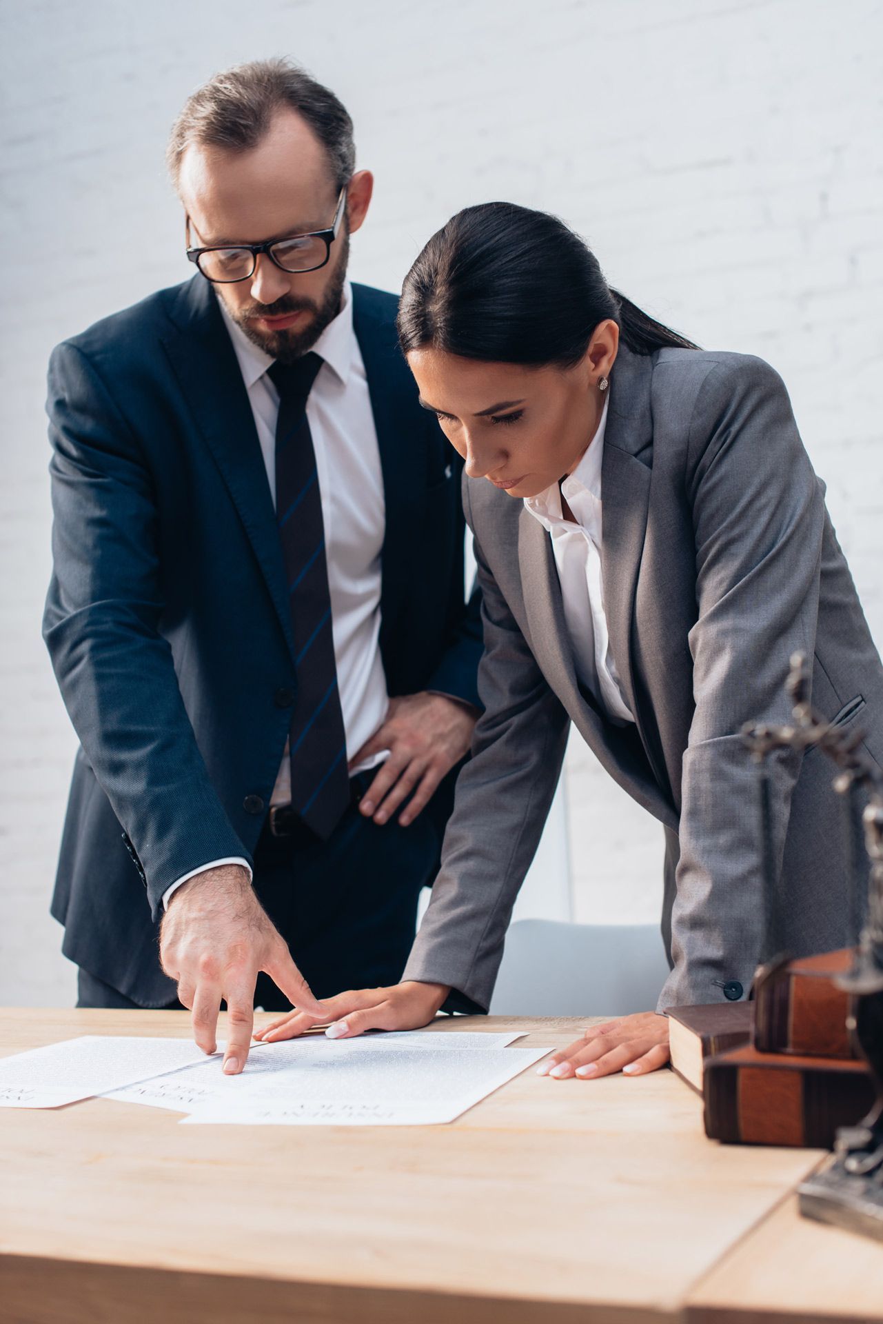 Two professionals in suits reviewing documents at a desk; man points, woman looks on.