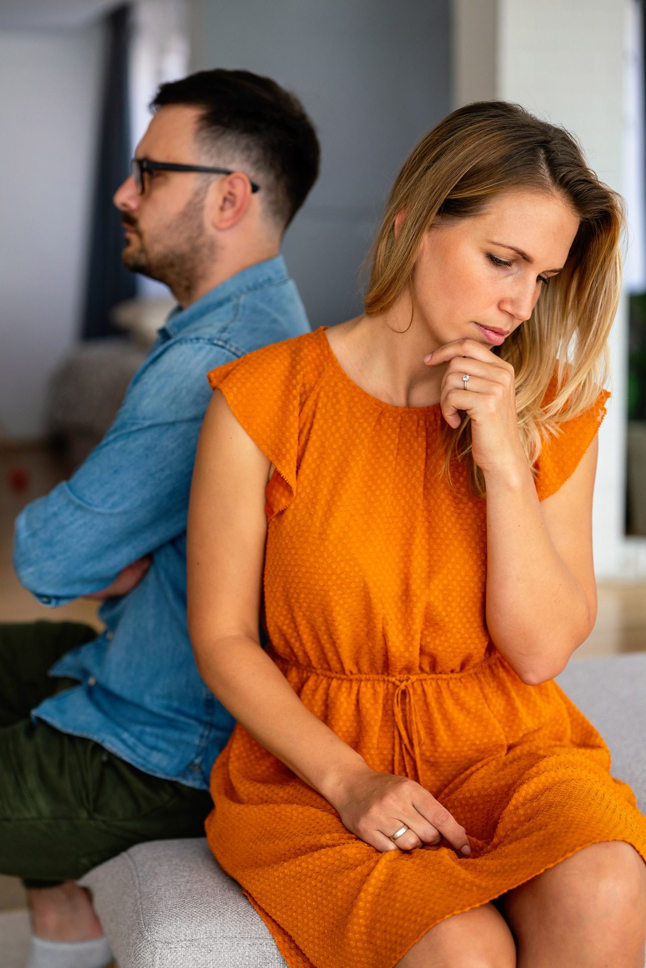 Man and woman sit back-to-back, looking away from each other.