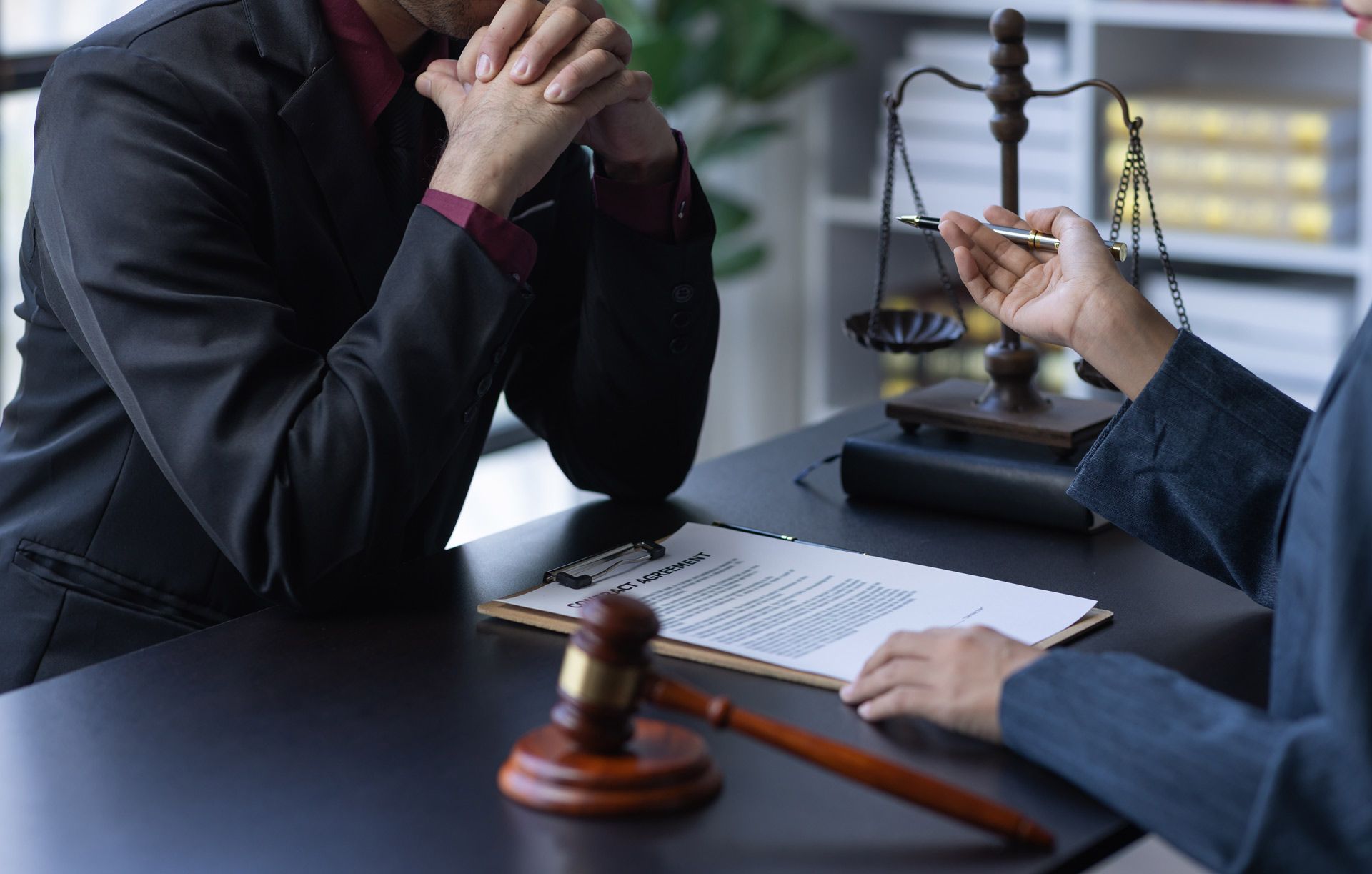 A lawyer pointing to a document, discussing with a client in an office setting, with a gavel and scales of justice present.
