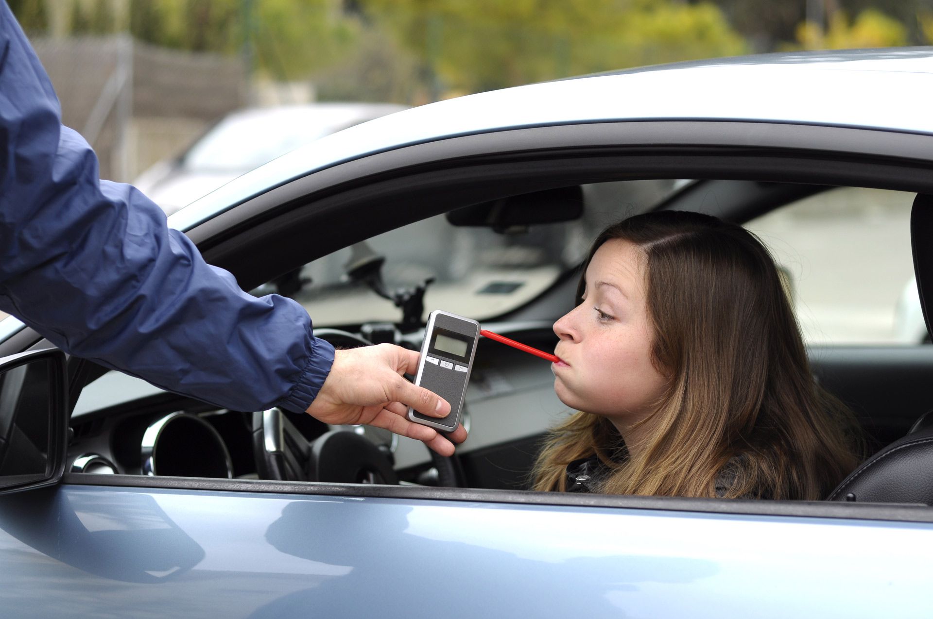 Woman in car taking breathalyzer test from police officer.