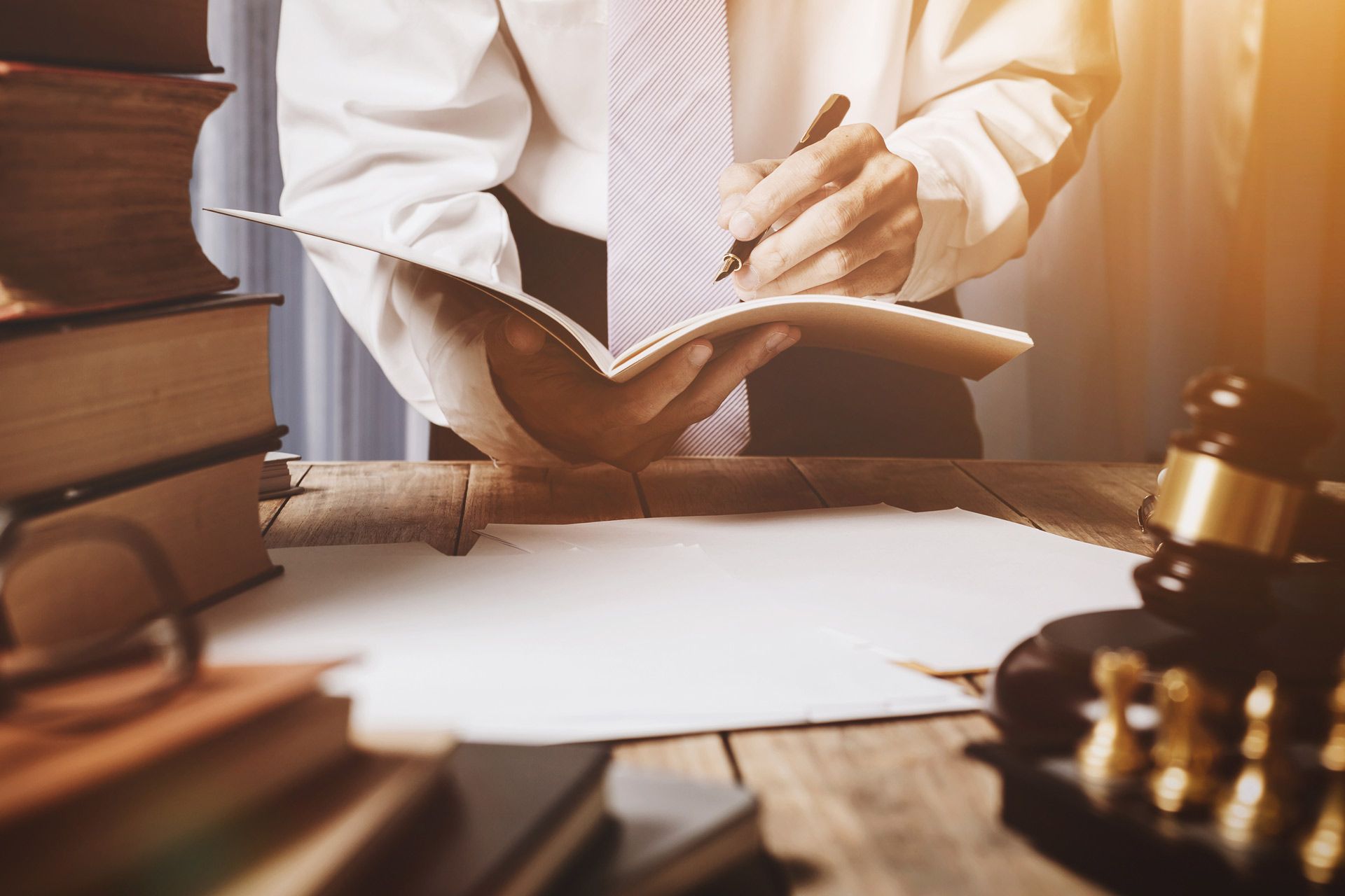 Lawyer writing in a notebook, surrounded by books, a gavel, and documents.