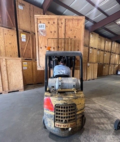 Two movers pushing a large, wrapped item on a dolly down a ramp into a moving truck. Outdoors.