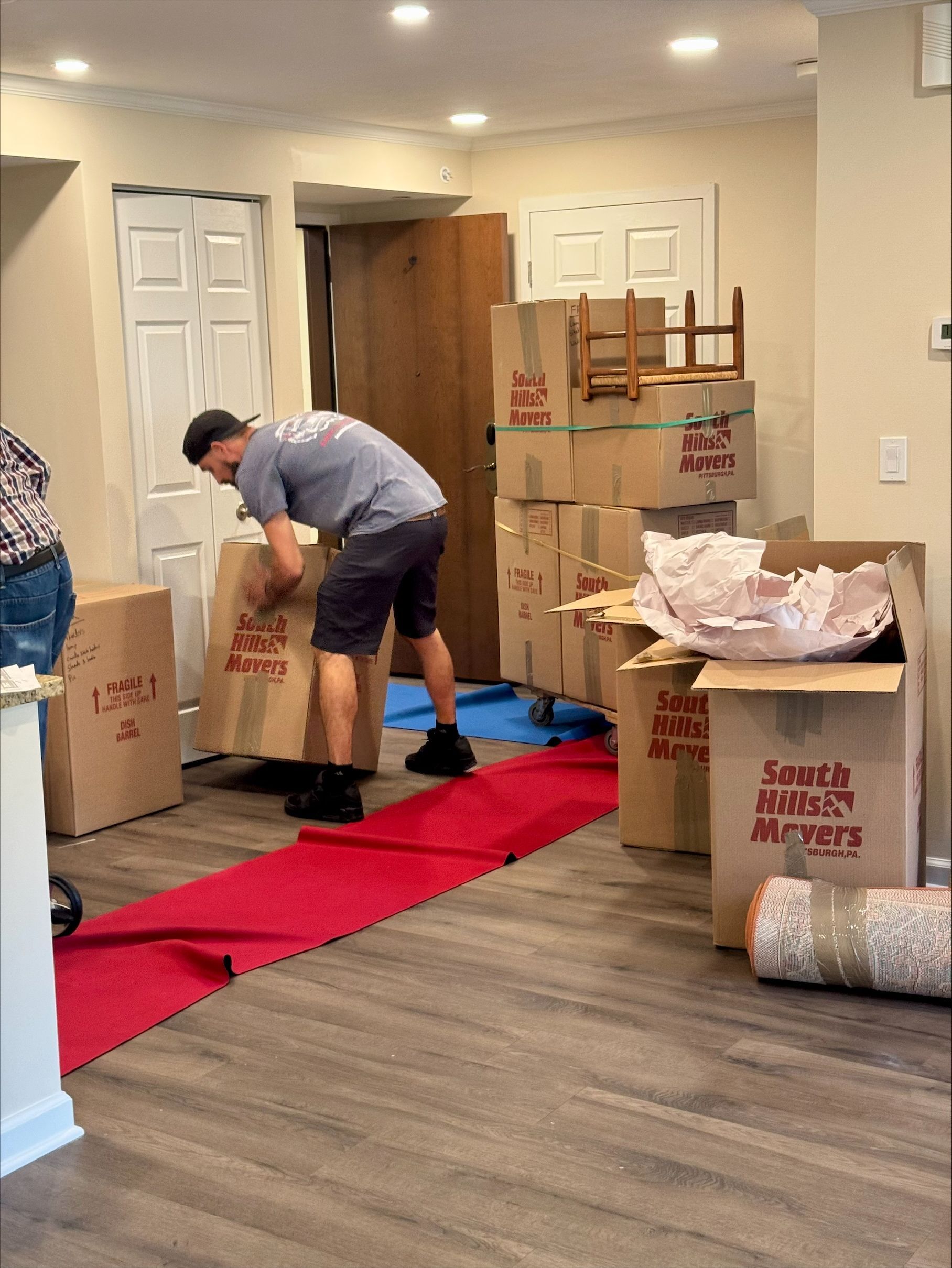 Man packing boxes in a room with moving supplies and a red runner, readying for transport.