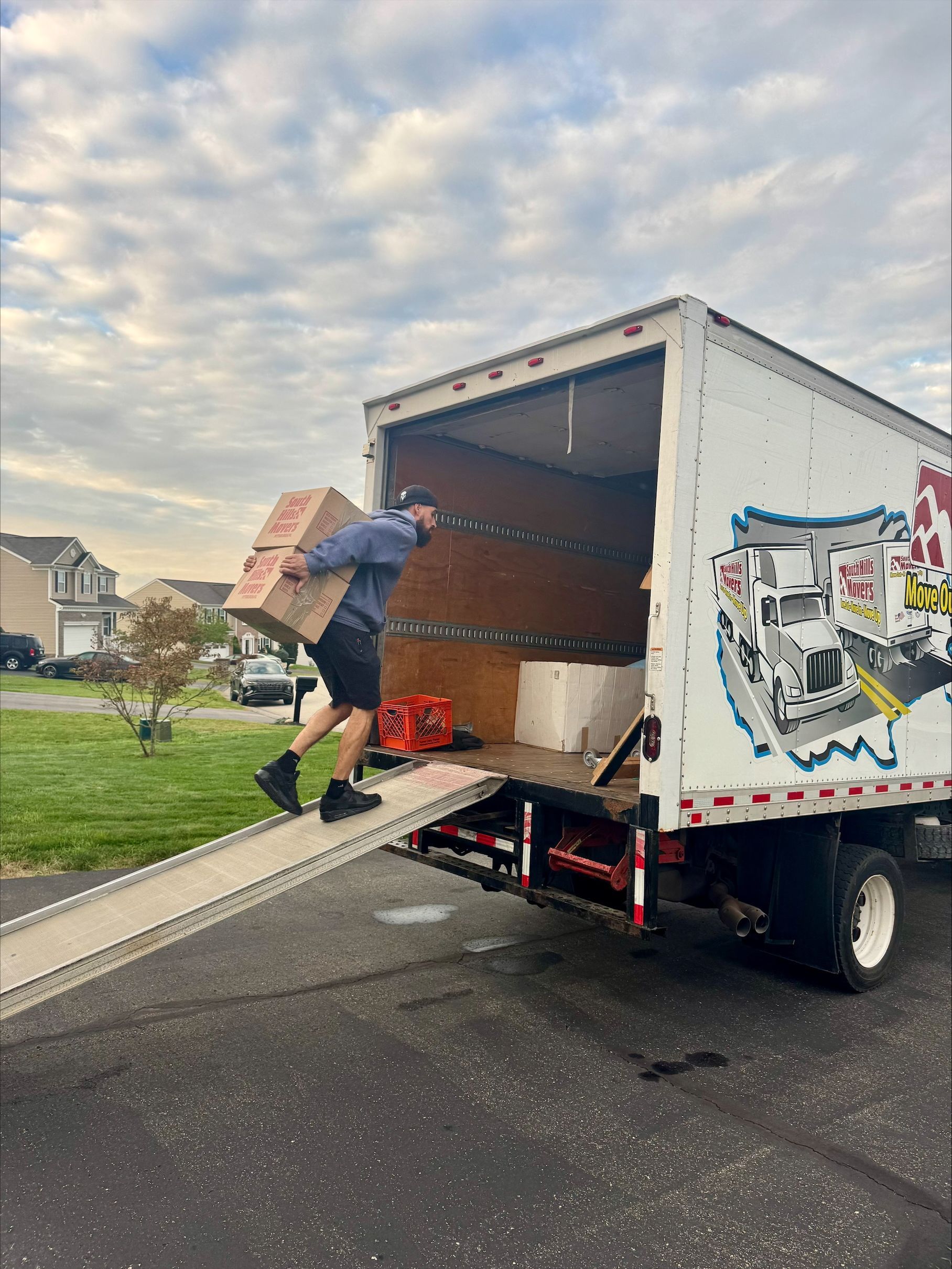 A person carries a box up a ramp into a moving truck parked on a residential street.