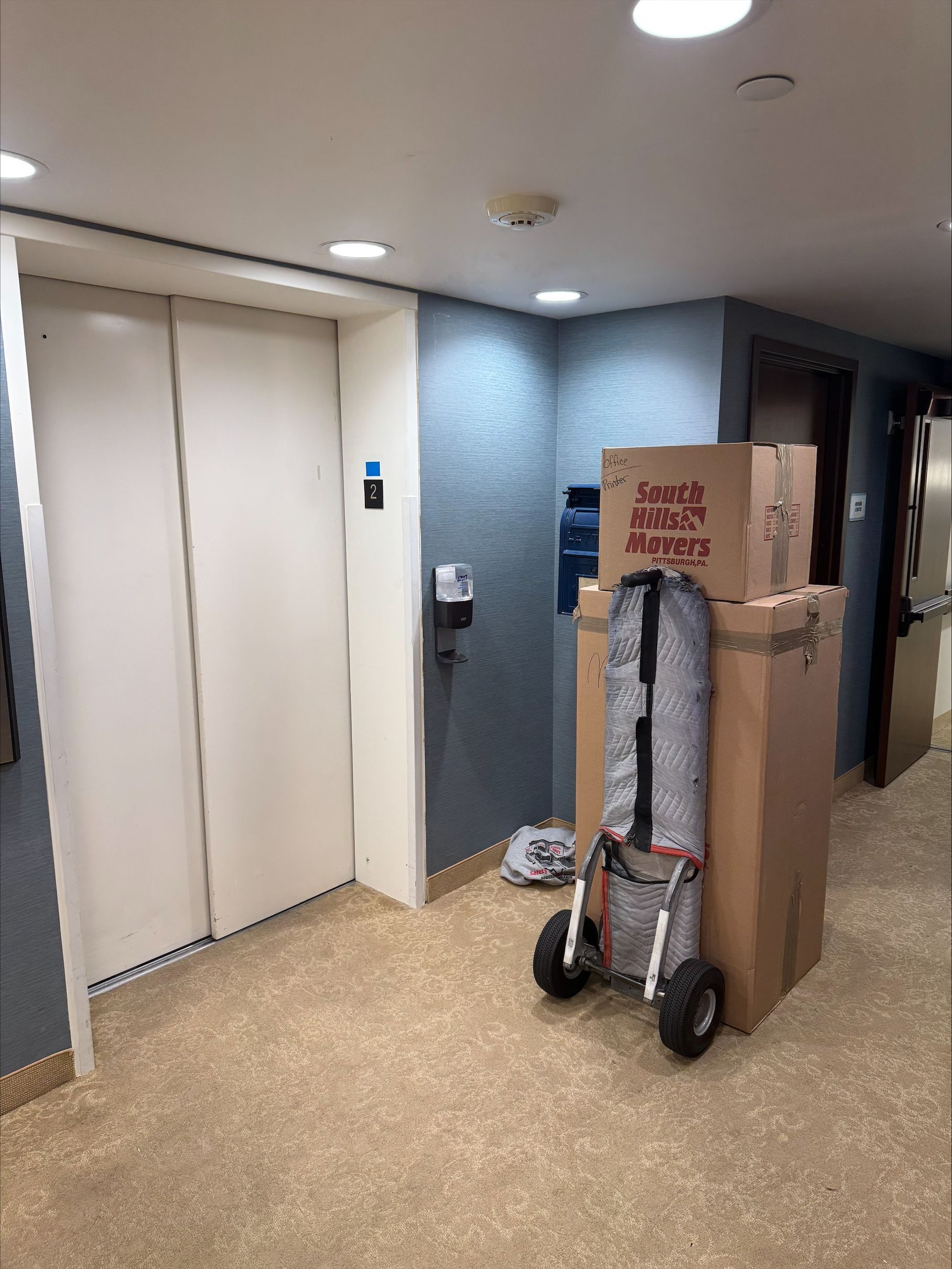Hallway with elevator, moving boxes, and a folding cart.