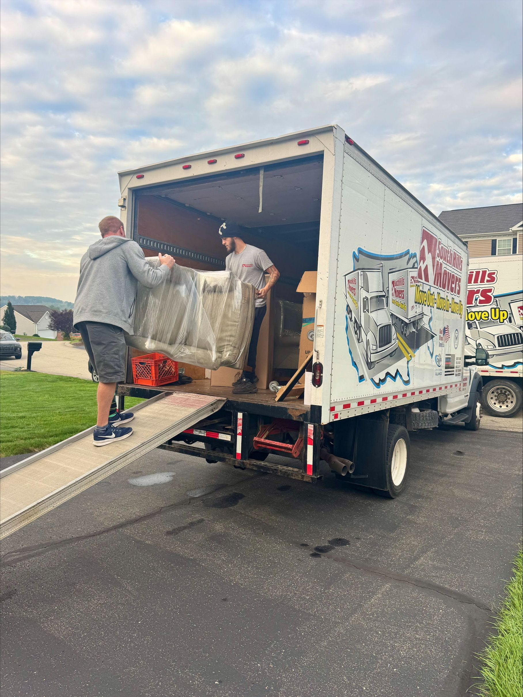 Two movers loading furniture onto a white moving truck from a residential driveway.