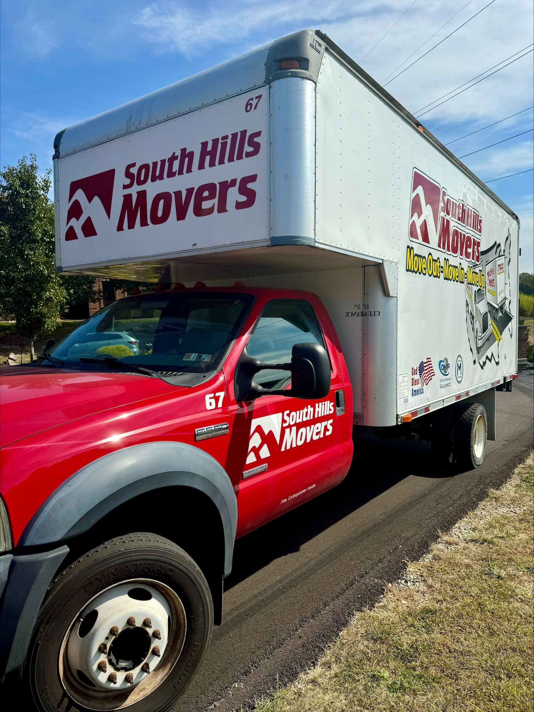 Red and white South Hills Movers truck on a road, under a blue sky.