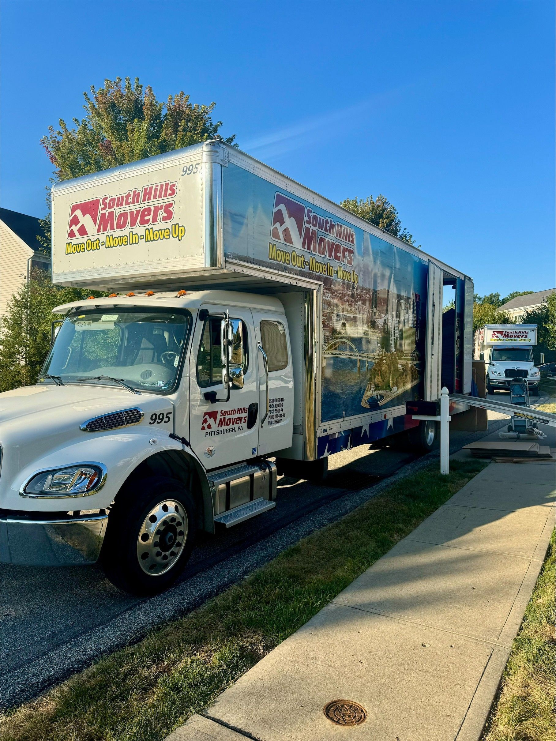 White moving truck with colorful art on the side parked on a road next to a sidewalk.