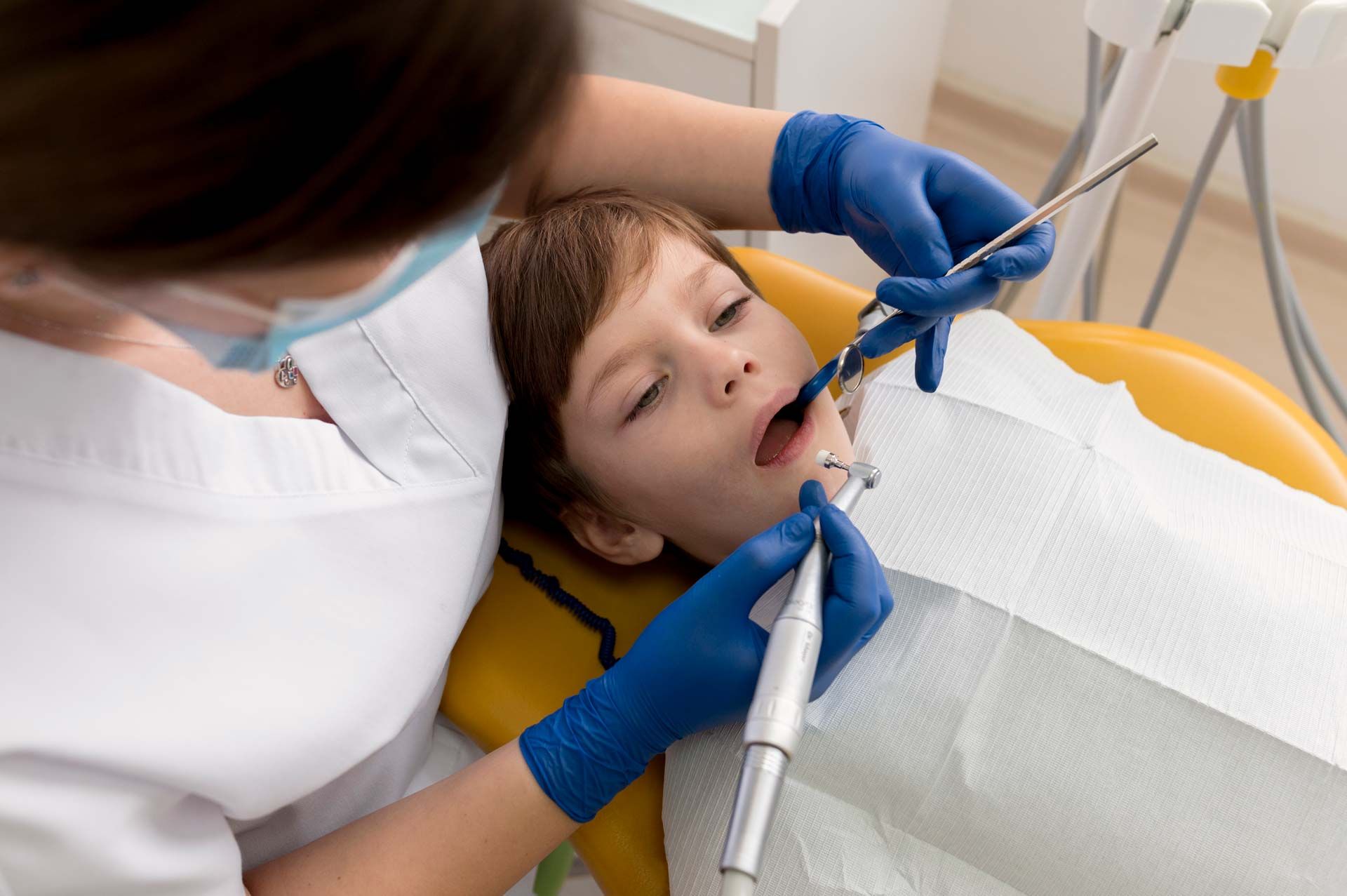 Dentist examining a child's teeth in a dental chair. The dentist wears blue gloves and a white uniform. Dentist examining a child's teeth in a dental chair. The dentist wears blue gloves and a white uniform.